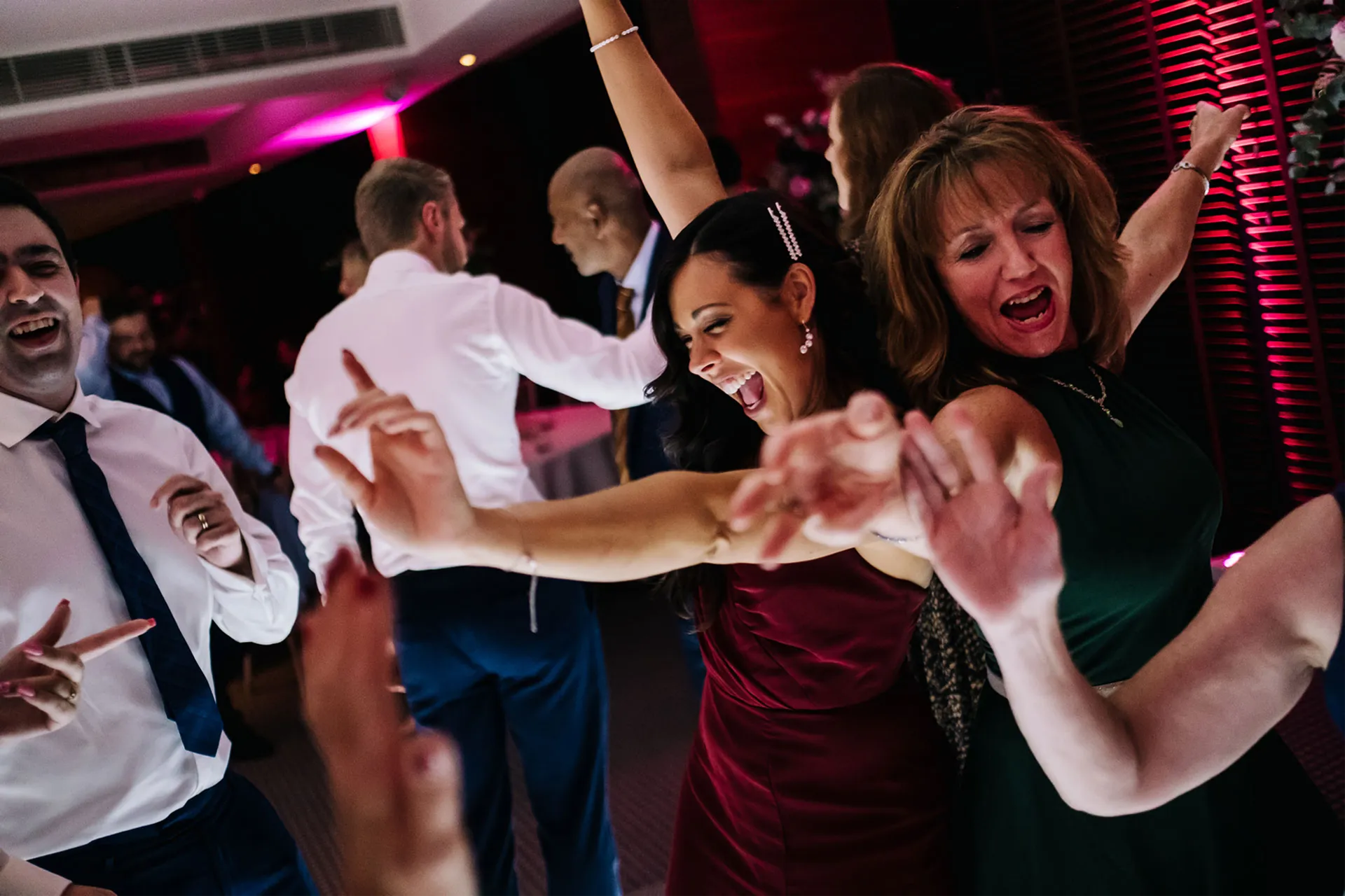 The image depicts joyful wedding guests dancing on the dance floor to popular wedding party songs. The lively atmosphere captures the essence of a wedding reception, where everyone is eager to dance and celebrate together.